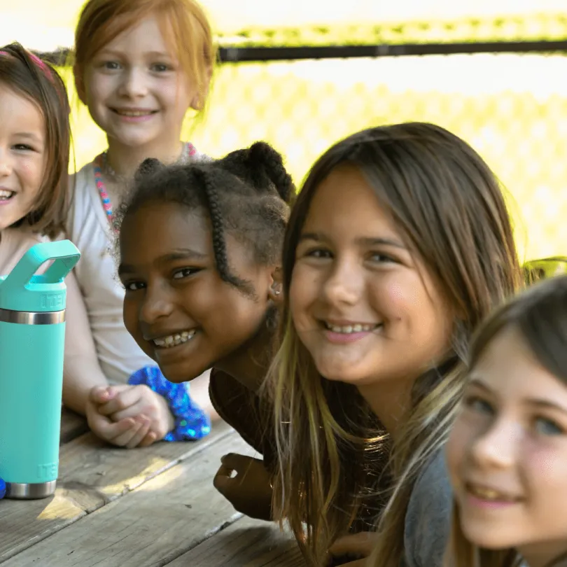 A group of five elementary age girls smile at the camera as they sit outside in an afterschool program.