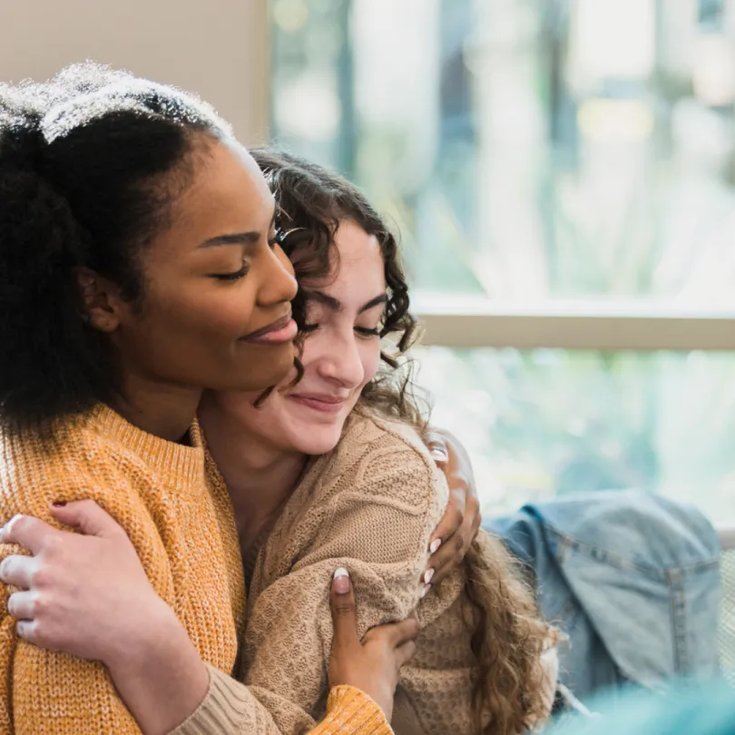 Two teenage girls hug each other as they sit in a teen support group session.