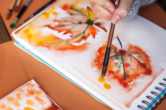 A close up of someone painting watercolor leaves.