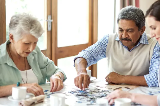 A group of seniors do a puzzle together and drink coffee.
