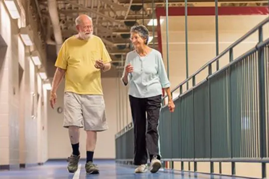 Two seniors talk while walking on an indoor track.
