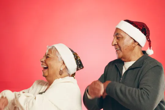 A senior couple dance together during the holidays. They are both wearing Santa hats.