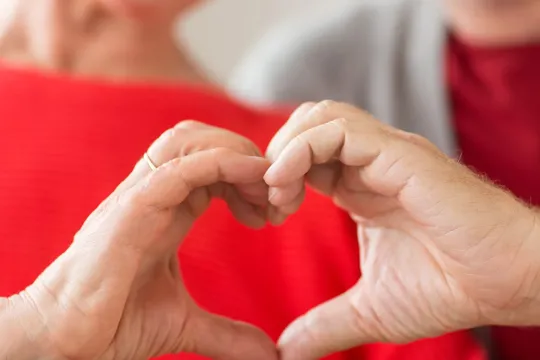 Two older adults put their hands together to make the shape of a heart.