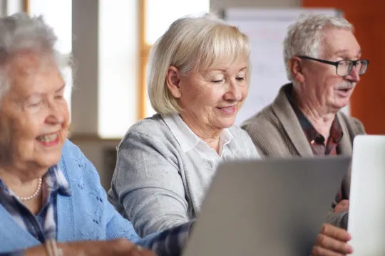 A group of older adults use laptops in a technology workshop.