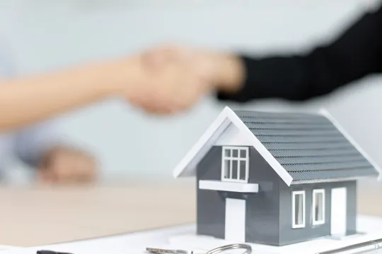 Two people shake hands over a real estate contract.