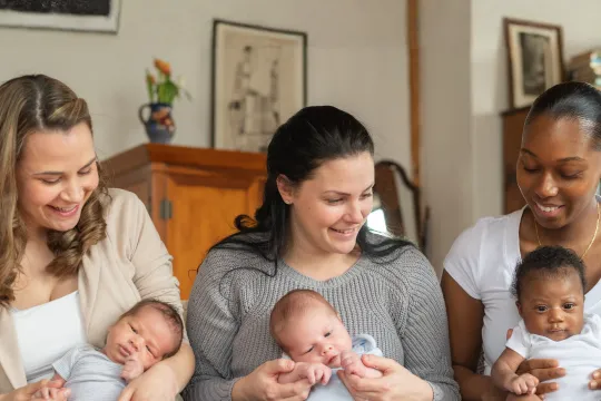 Three mothers with babies sit together in a postpartum support group.