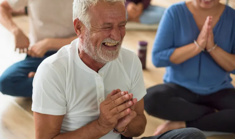 A man laughs while doing yoga in a group class.