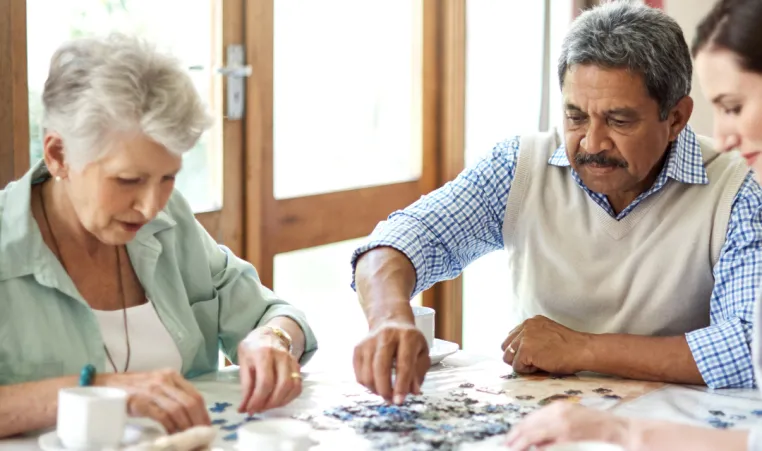 A group of seniors do a puzzle together and drink coffee.