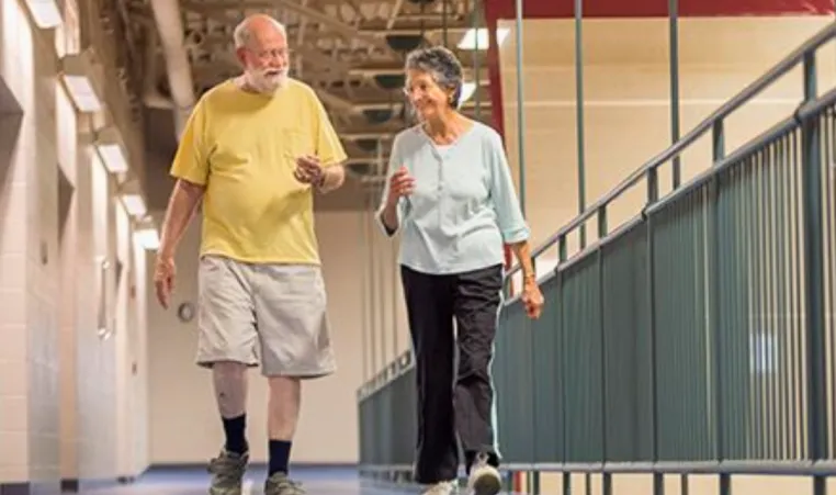 Two seniors talk while walking on an indoor track.