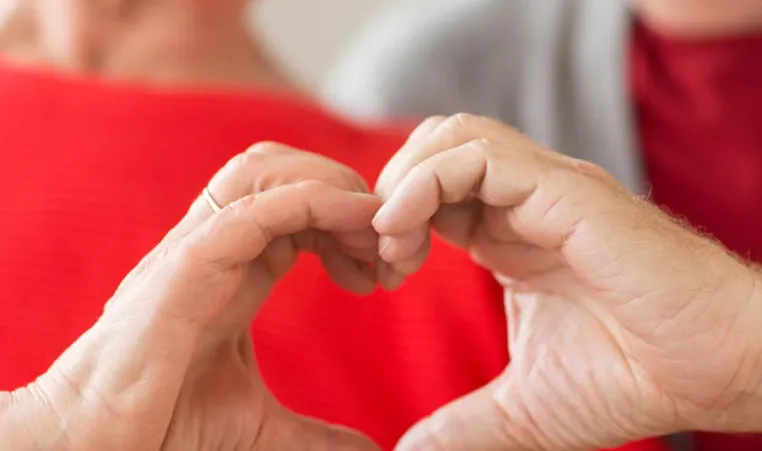 Two older adults put their hands together to make the shape of a heart.