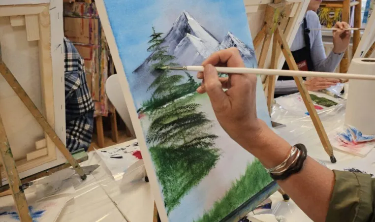 A close-up of someone painting in a Bob Ross painting class.