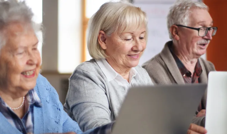 A group of older adults use laptops in a technology workshop.
