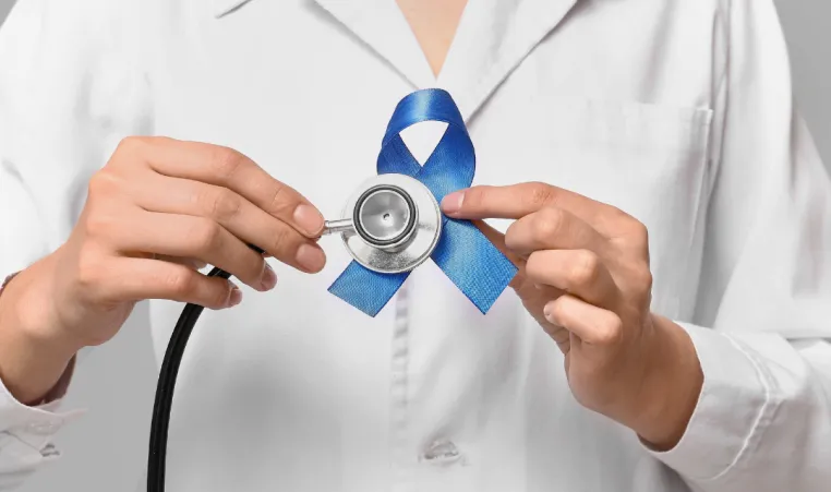 A doctor holding a blue cancer ribbon and a stethoscope.