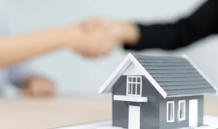 Two people shake hands over a real estate contract.