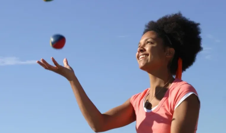 A woman smiles as she learns how to juggle.
